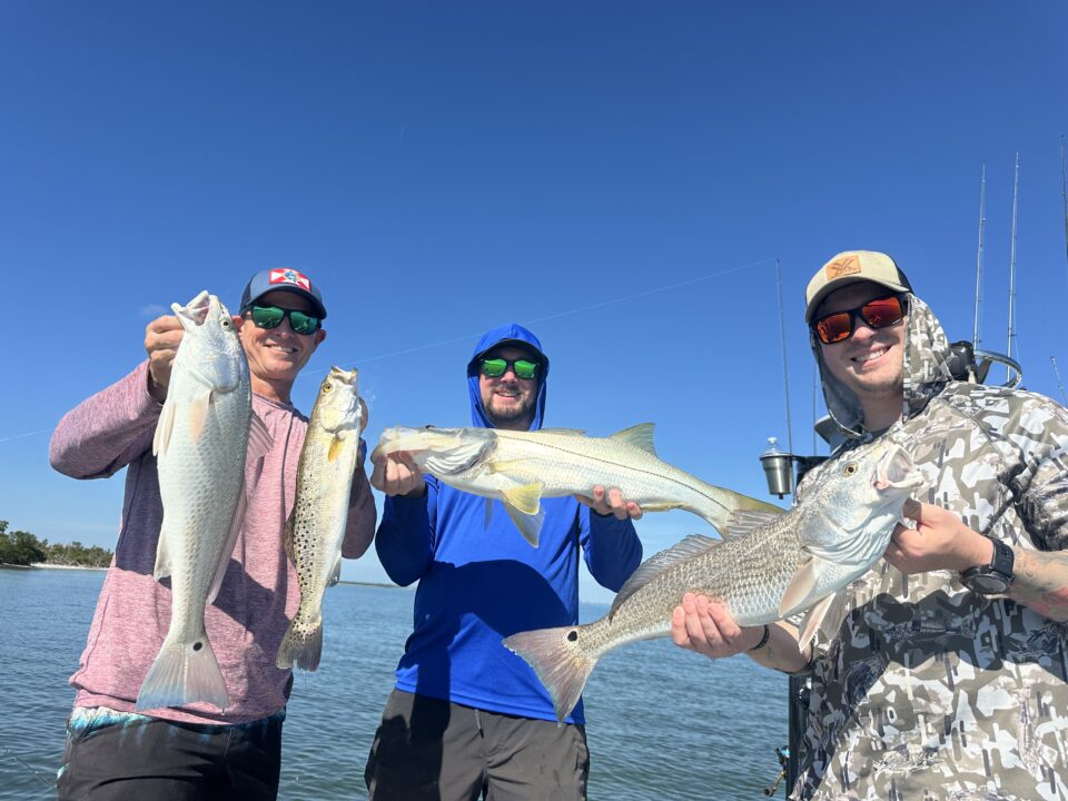 Group of anglers holding redfish, snook, and trout during a successful December inshore fishing trip in Boca Grande.