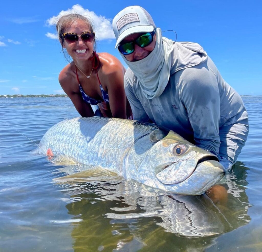 Boca Grande Tarpon Fishing – Captain Danny Landing a Trophy Tarpon Captain Danny and a female angler releasing a large Tarpon in shallow water during a Boca Grande Tarpon fishing charter with ReelFishing Charters