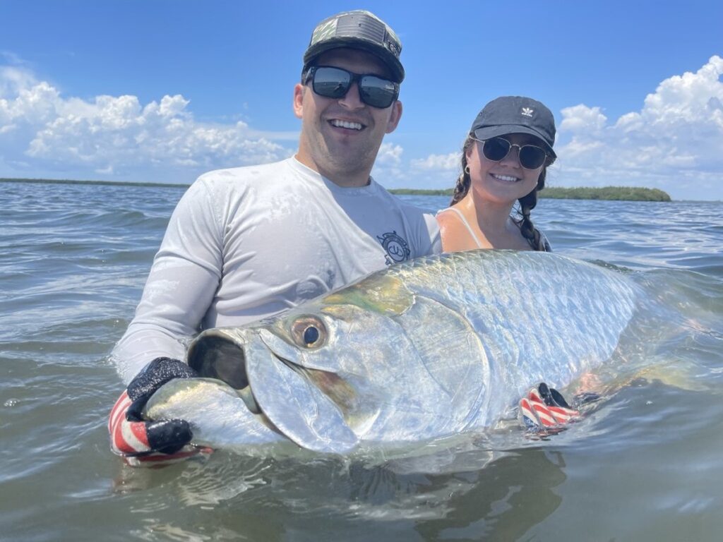 Boca Grande Tarpon Fishing – Happy Anglers Landing a Trophy Tarpon A couple releasing a large Tarpon in shallow water during a Boca Grande Tarpon fishing charter with ReelFishing Charters.