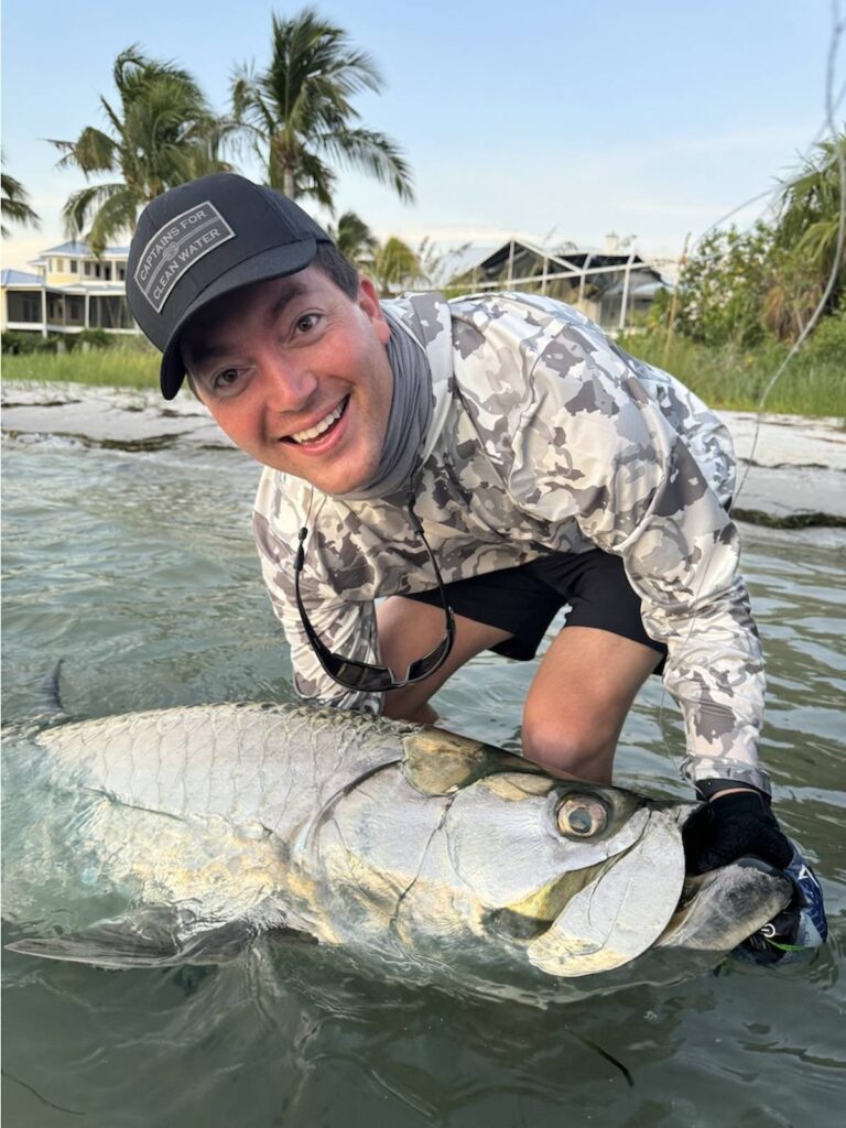Massive Tarpon Caught Near Boca Grande – ReelFishing Charters Angler holding a large tarpon in shallow water near Boca Grande during a ReelFishing Charters trip
