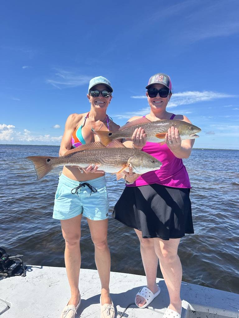 Cape Coral Fishing Charters – Redfish Double Catch with ReelFishing Charters Two lady anglers holding Redfish during an inshore fishing charter in Cape Coral with ReelFishing Charters