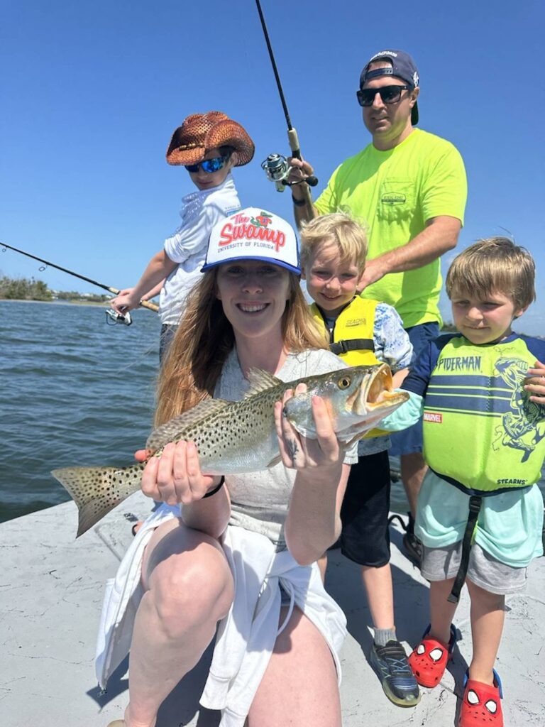 Family Fishing Fun in Fort Myers – ReelFishing Charters Family fishing charter in Fort Myers with ReelFishing Charters – woman holding a speckled trout with children and guide on the boat